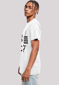Tricou alb din bumbac cu text negru îndrăzneț și o grafică cu urechi de iepure deasupra unor dungi orizontale. Mâneci scurte și croi lejer.