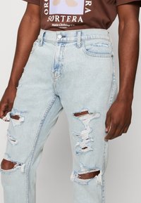 Ljusblå slitna jeans i denim med stora slitna lappar, rak ben-design och en klassisk fem-fack konstruktion.