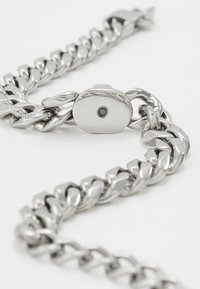 Hopeaketju käsikoru, jossa on toisiinsa kytkeytyviä lenkkejä, ja jossa on suorakulmainen kiinnitys, jossa on pieni musta piste ykistyiskohdassa.