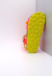 Sandale rose vif avec une semelle extérieure texturée jaune. Elle dispose de brides réglables et d'une construction robuste. Conçue pour le confort et la durabilité.