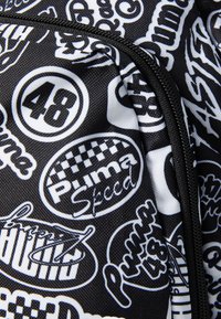 Black fabric bag featuring an all-over print of white logos, including "Puma," "Speed," and circular designs with numbers and patterns.