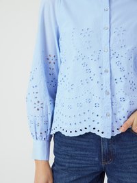 Light blue cotton shirt with floral eyelet embroidery, scalloped hem, and long puff sleeves. Button-down front and cuff detailing.