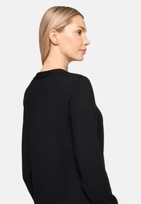 Schwarzer Strickpullover mit Rundhalsausschnitt und langen Ärmeln, der eine glatte Textur und eine figurbetonte Passform aufweist, seitlich betrachtet.