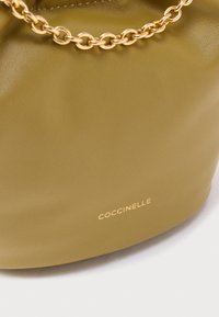 Kožená kabelka olivově zelené barvy s hladkou texturou, vybavená řetízkovým popruhem v zlatém tónu a raženým logem na boku.