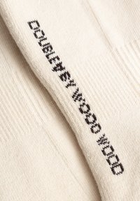 Nærbillede af hvidt stof med sort broderet tekst "Daily wooob mood" på en foldet strikket overflade.