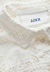 Col de blouse en dentelle blanche brodée avec bouton et étiquette en tissu indiquant le nom de la marque "JJXX".