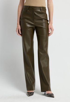 Olijfgroene neplederen broek met een hoge taille, voorzakken en een gladde afwerking, gecombineerd met puntige zwarte hakken.