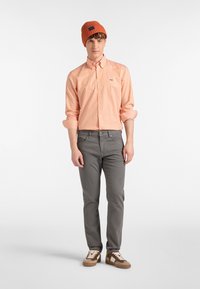 Orange- och vitrandig skjorta med knappar, grå byxor och bruna sneakers. Avslutad med en texturerad orange stickad mössa med ett märke.