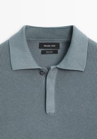 Polo de couleur bleu discret, en 100 % coton, avec un motif en maille texturée, patte courte et fermeture à deux boutons.