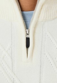 Balts adīts džemperis ar rāvējslēdzēja apkakli, kuram ir ribota tekstūra un dimanta raksti. Rāvējslēdzēju papildina melna cilpa. Iekšējā kārta ir gaiši zila.