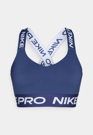 Jūras zils sporta krūšturis ar platu elastīgu joslu un baltām krusteniskām siksnām, uz kurām ar lieliem burtiem rakstīts "NIKE".