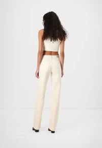 Witte cropped top gecombineerd met crèmekleurige, hooggetailleerde, rechte broek met een eenvoudig ontwerp en subtiele achterzakken.