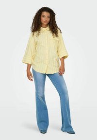Gulrandig skjorta med knappar, bröstficka, vida ärmar, kombinerad med ljusblå utsvängda jeans och spetiga skor.