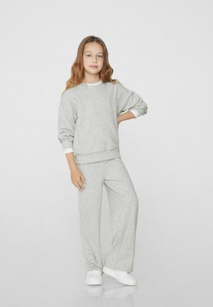 Jasnoszare dresy i oversize'owa bluza z miękkiego materiału, z okrągłym dekoltem i długimi rękawami z białymi akcentami.