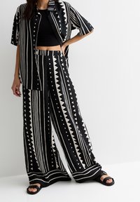 Zwart-wit samengestelde set met een korte mouwen shirt en wijde broek met een geometrisch patroon van strepen en driehoeken.