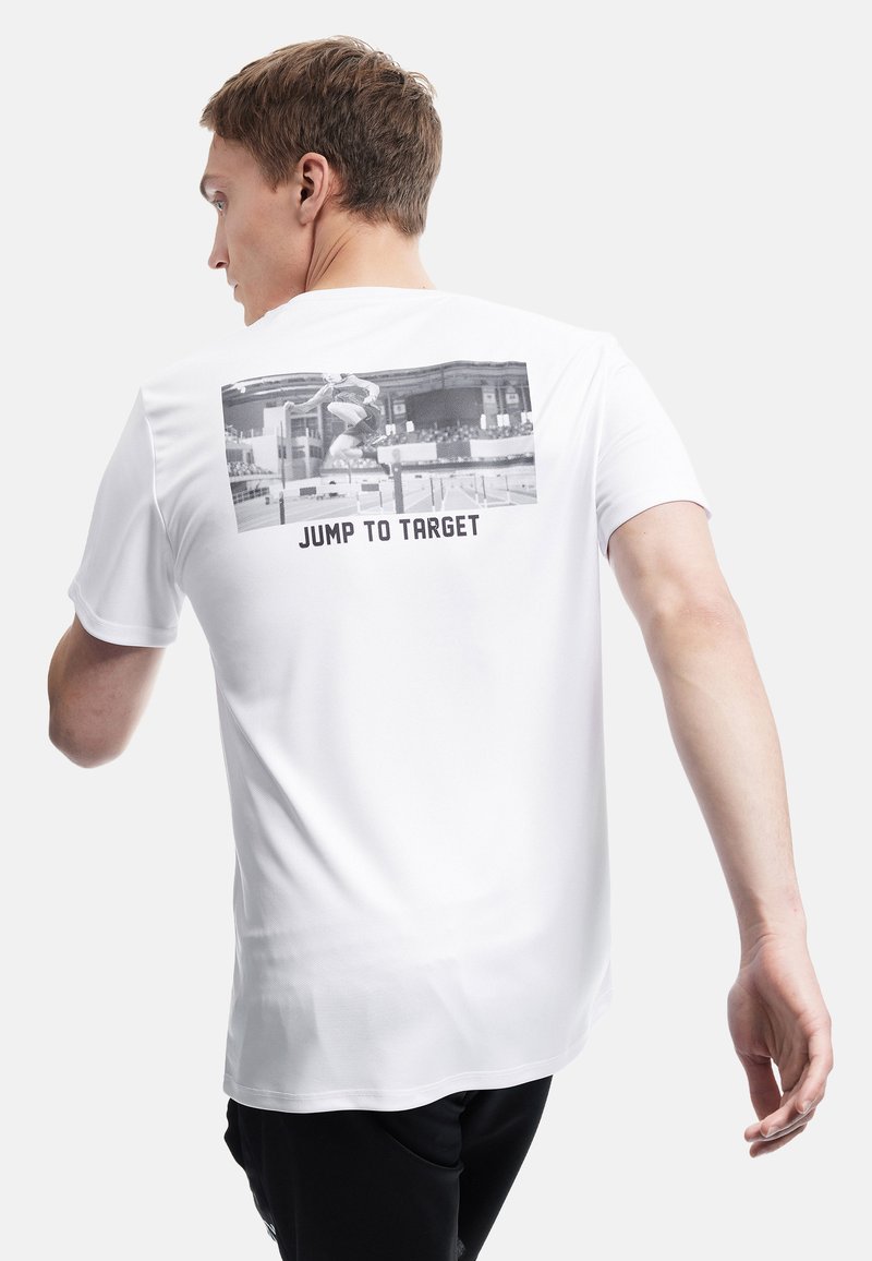 Camiseta atlética blanca con un gráfico trasero de un saltador en acción y el texto "SALTA AL OBJETIVO" debajo, de manga corta y textura suave.