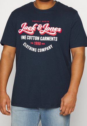 Mand iført navy blå Jack & Jones t-shirt med hvid og rød tekst, kombineret med lyseblå denim jeans.