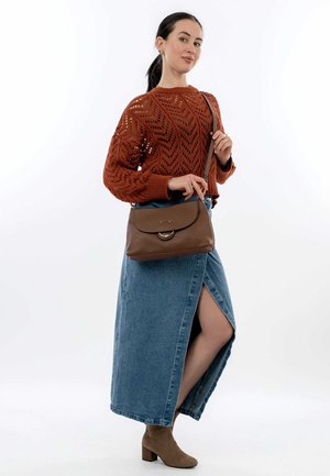 Maglione lavorato a maglia bronzo con motivo a zig zag, gonna maxi in denim con spacco laterale e stivaletti beige alla caviglia, mentre tiene una borsa a tracolla in pelle marrone.