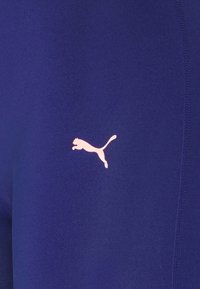 Leggings sportivi Puma in tessuto blu scuro uniforme con una texture liscia. Presentano un logo rosa di un gatto saltante sul lato.