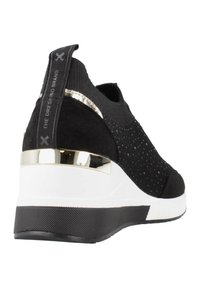 Zapatilla deportiva negra con textura de punto, acento dorado metálico en el talón, media suela blanca y suela de goma con patrón.