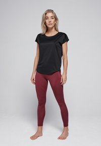 Zwart kortmouwen top gecombineerd met bordeauxrode leggings met rode stiksels, met een aansluitend ontwerp gemaakt van rekbaar materiaal.