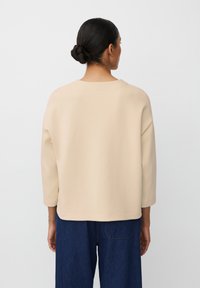 Beżowy sweter z luźnym krojem, 3/4 rękawami, okrągłym dekoltem i miękką fakturą, w zestawie z ciemnoniebieskimi spodniami o szerokich nogawkach.