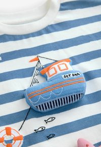 Weißes T-Shirt mit blauen horizontalen Streifen, mit einer strukturierten, gestickten Boot-Applikation in Blau, Orange und Weiß, die Fischdetails enthält.