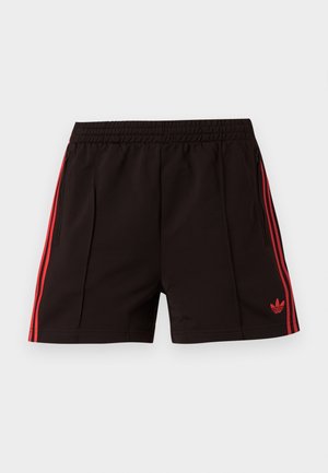 Mustat urheilushortsit, joissa on joustava vyötärö, punaiset sivuraidat, vetoketjulliset taskut ja punainen Adidas Trefoil -logo vasemmassa lahkeessa.
