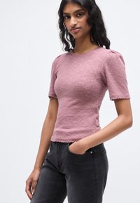 Εφαρμοστό τοπ με κοντά μανίκια από ριμπ ύφασμα σε ξεθωριασμένο ροζ απόχρωση, με κυματιστό τελείωμα και διακριτικά φουσκωτά μανίκια, σε συνδυασμό με μαύρο παντελόνι τζιν.