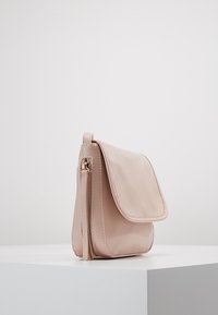 Hellrosa Leder-Crossbody-Tasche mit Klappenverschluss, seitlichem Reißverschluss und Quasten-Detail. Glatte Textur und kompakte rechteckige Form.