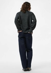 Grå stickad tröja med rund halsringning, ribbstickade muddar och fåll, kombinerad med mörkblå jeans med raka ben och svarta skor.