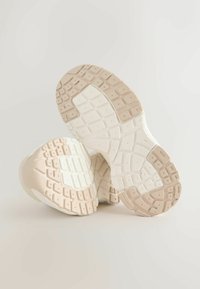 Sneakers con suola in gomma bianca e beige chiaro, caratterizzata da una superficie testurizzata con motivi rettangolari e una base imbottita per supporto.