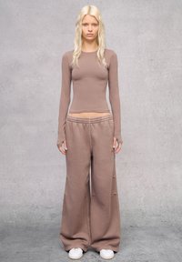 Langarm, aansluitend T-shirt en brede sweatpants in lichtbruine stof. De broek heeft een elastische tailleband, beide stukken zijn glad en zacht.