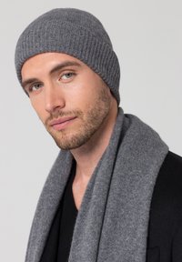 Grijze gebreide beanie met ribbelstructuur, gecombineerd met een bijpassende grijze sjaal, die om de nek hangt. Beide items hebben een zachte, warme uitstraling.