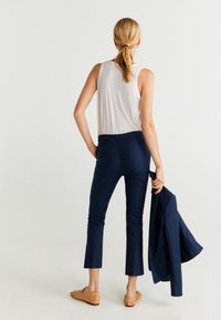 Námořnicky modré zkrácené kalhoty se dvěma zadními kapsami, v kombinaci s bílým tílkem. Námořnicky modré sako přehozené přes jedno rameno; světle hnědé baleríny.