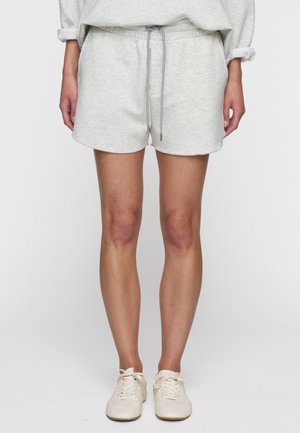 Shorts in cotone grigio chiaro, morbidi, con vita elastica, cordino regolabile e orlo curvo. Abbinati a scarpe beige con lacci.