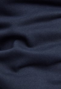 Tissu bleu marine foncé avec des plis doux et une texture fine en tricot visible créant des ombres et des reflets délicats.