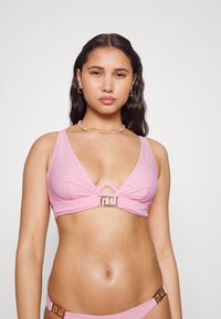 Top de bikini rosa com decote profundo, alças largas e detalhes em metal dourado no centro e nas laterais. Textura suave.