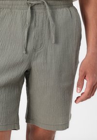 Shorts vert olive clair en tissu texturé, dotés d'une taille élastique avec cordon de serrage et de poches latérales.