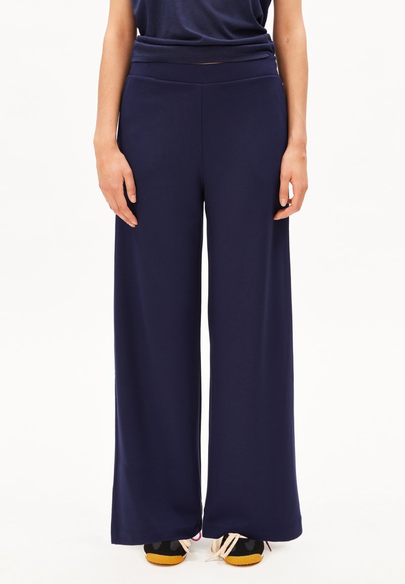 Marineblaue Hosen mit weitem Bein aus glattem Stoff und hoher Taille. Sie zeichnen sich durch ein schlichtes Design, einen geraden Schnitt und eine weiche Textur aus. Kombiniert mit dunklen Schuhen.