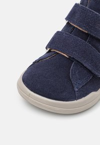 Scarpa velcro blu navy con tomaia in morbido suede e finitura texturizzata. Suola in gomma mostrata, con punta arrotondata e dettagli di cucitura.