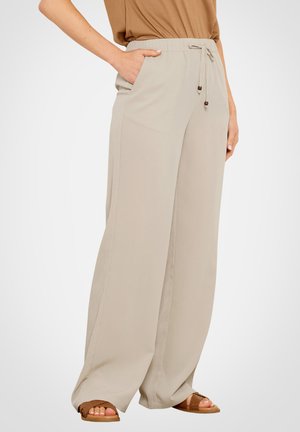 Femme portant un pantalon large beige avec taille à cordon de serrage et poches latérales, assorti à des sandales marron et un haut marron.