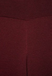 Detailný záber vinočerveného rebrovaného pleteného materiálu s V-švom a hrubším rebrovaným pásom na vrchu.