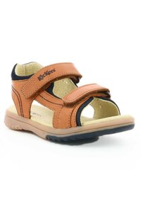 Sandal de cuero marrón con dos correas ajustables de Velcro, diseño de punta abierta, plantilla acolchada y suela de goma texturizada en azul oscuro.