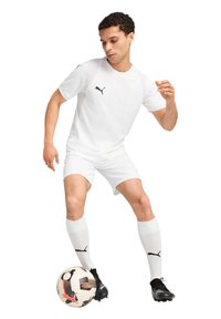Weißes Sportshirt und Shorts, schwarzes Logo auf der Brust, kombiniert mit weißen kniehohen Socken und schwarzen Fußballschuhen, dazu ein gemusterter Fußball.