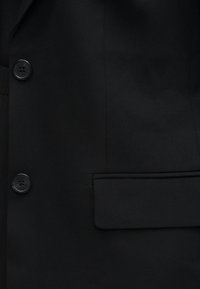 Μαύρο σακάκι κοστουμιού με λείο, υφασμάτινο υλικό, δύο στρογγυλά κουμπιά και ένα ορθογώνιο τσέπη στην αριστερή πλευρά.