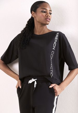 Schwarzes, oversized T-Shirt mit kurzen Ärmeln, das den weißen Text "FRENCH CONNECTION" vertikal an der Seite trägt. Weiches Material, lockere Passform.
