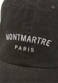 Cappellino in cotone nero con testo ricamato "MONTMARTE PARIS" in bianco, con visiera curva e tessuto testurizzato. Nessun ulteriore accento.