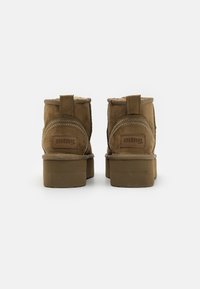 Botas de tobillo de ante marrón con un acabado texturizado, que cuentan con un pequeño tacón, detalles cosidos y una lengüeta en la parte posterior para facilitar su colocación.