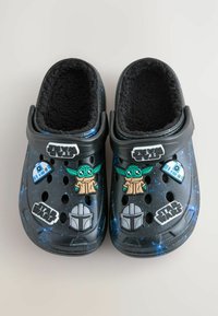 Zwarte instapschoenen met een zachte zwarte voering en verschillende Star Wars-thema versieringen, waaronder figuren en logo's, in een ruimtepatroon.